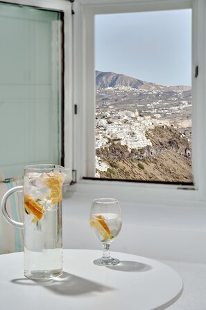 Una mesa con una jarrón y un vaso de agua, una ventana con vistas a un pueblo y montañas.