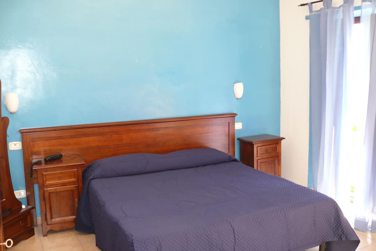 A bedroom with a wooden bed, a bedside table, a nightstand, and a wall-mounted lamp.