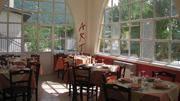 A dining area with tables set for meals, large arched windows, and a view of greenery outside. - Art Hotel (Villetta Barrea)