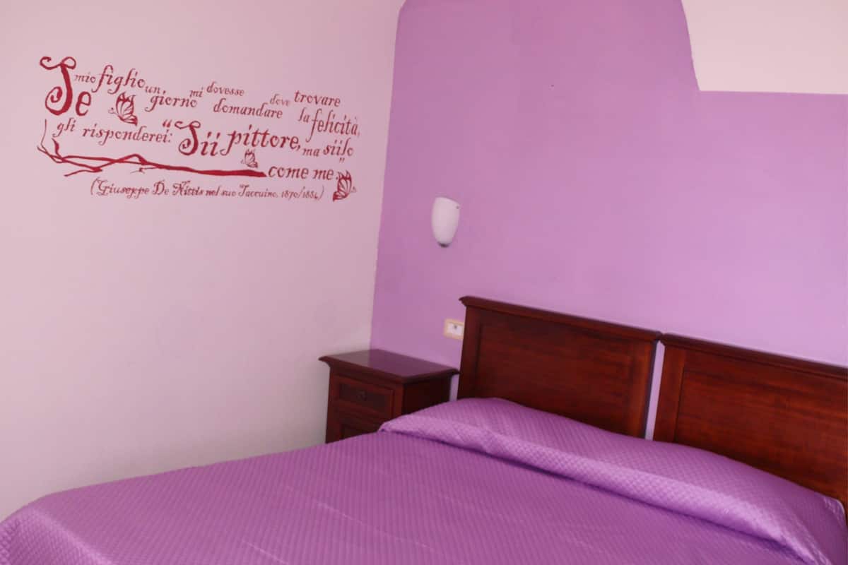 A bedroom with a bed, a nightstand, and a wall with a quote in Italian.