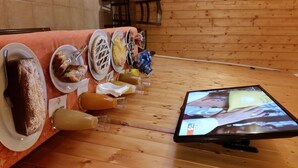 A table with various pastries and drinks, a television displaying a program, and a wooden floor. - Art Hotel (Villetta Barrea)
