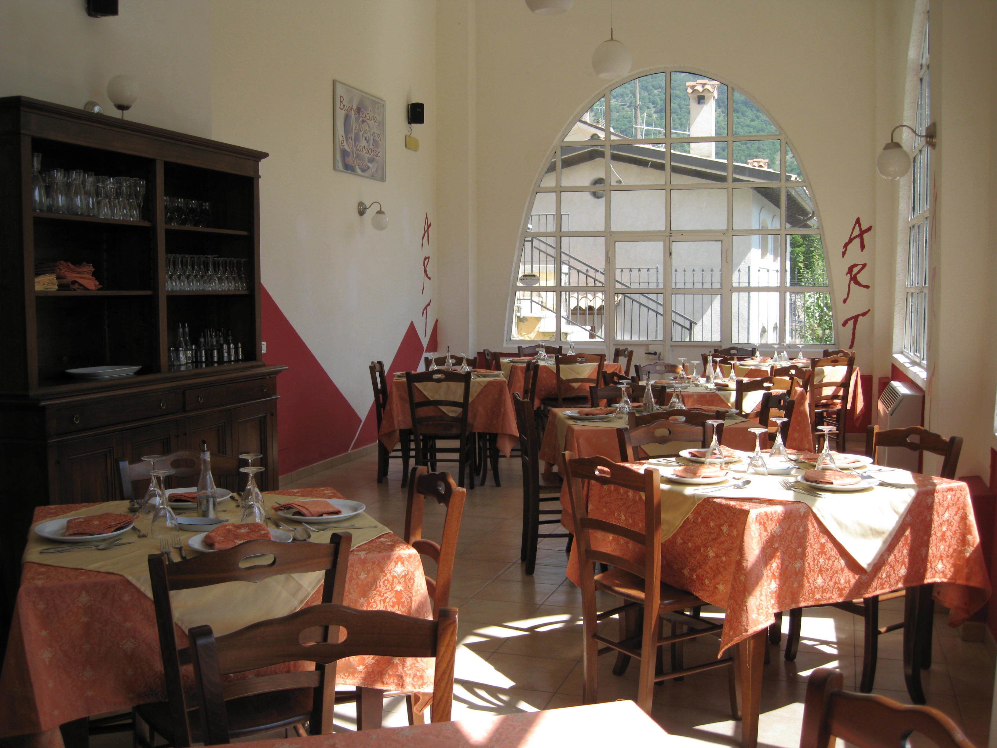 Un espace repas comprenant plusieurs tables et chaises, une bibliothèque et une grande fenêtre en arc de cercle.