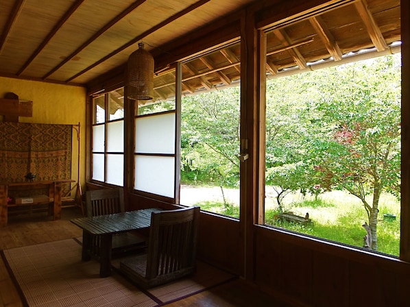 A traditional Japanese room with tatami flooring, a low table with a bench, and large windows offering a view of a garden.