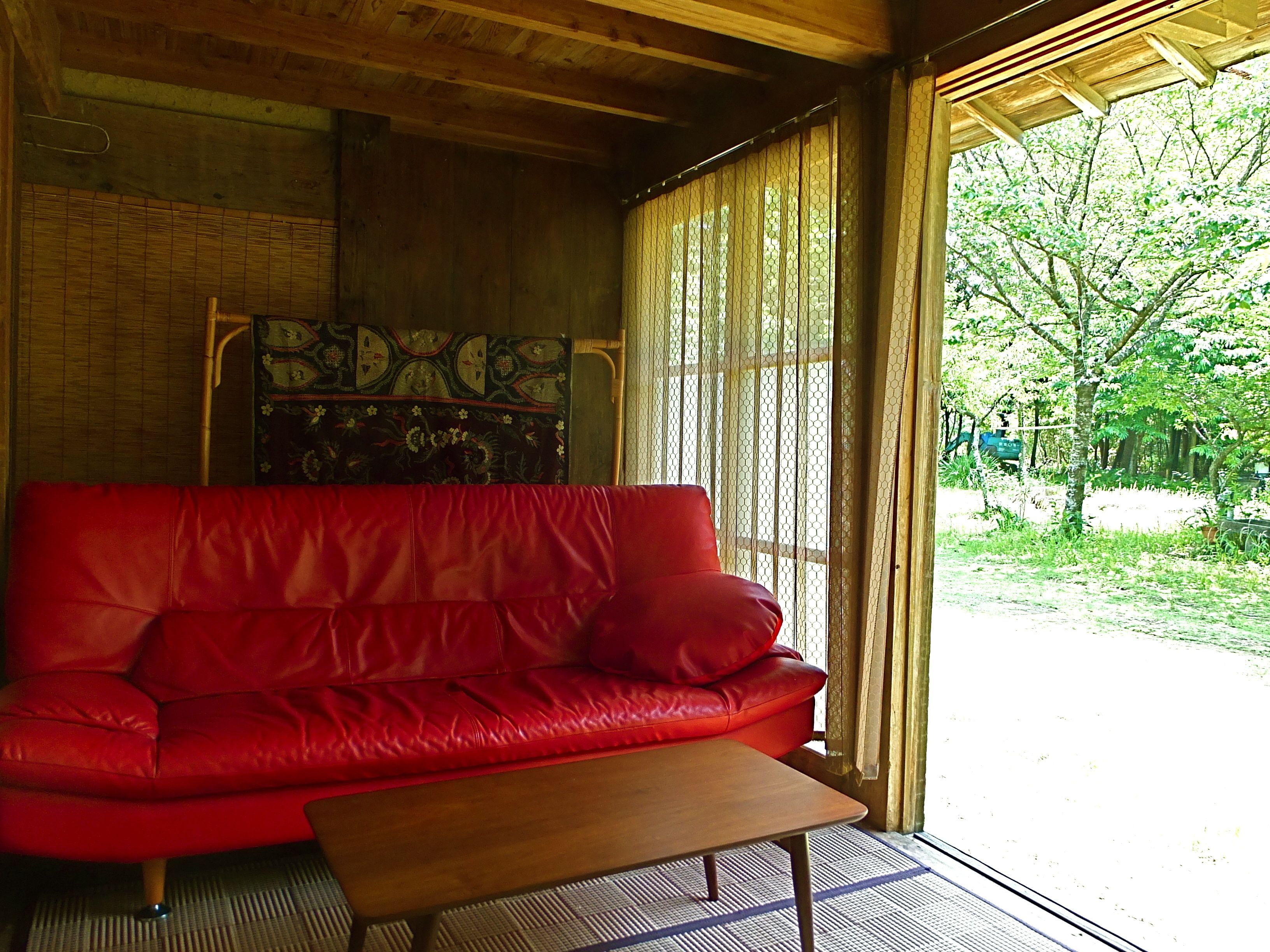 A red leather sofa and a wooden coffee table in a room with wooden beams and a view of greenery outside.