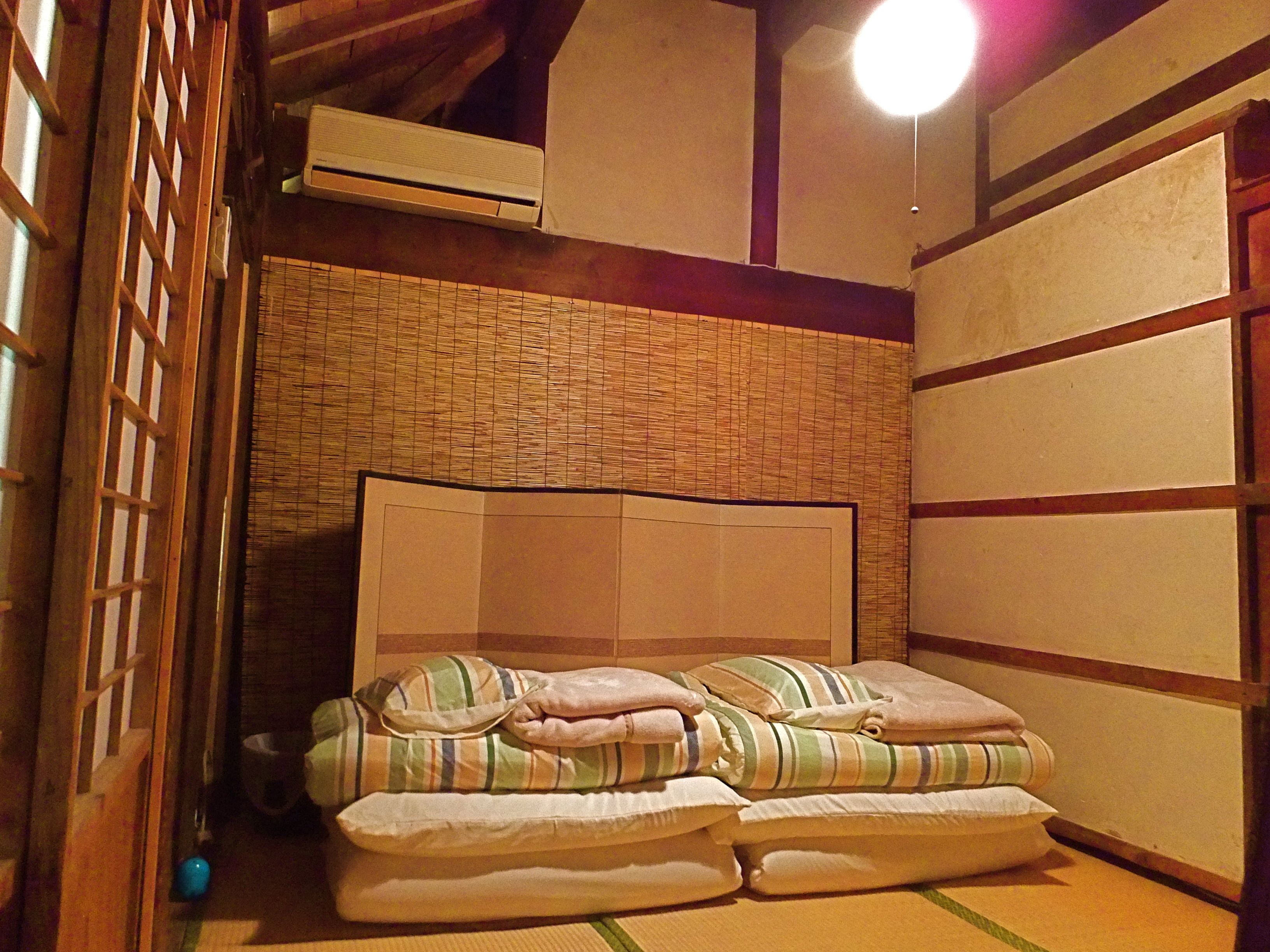 A traditional Japanese-style room with tatami flooring, a low wooden bed frame, and a shoji screen door.