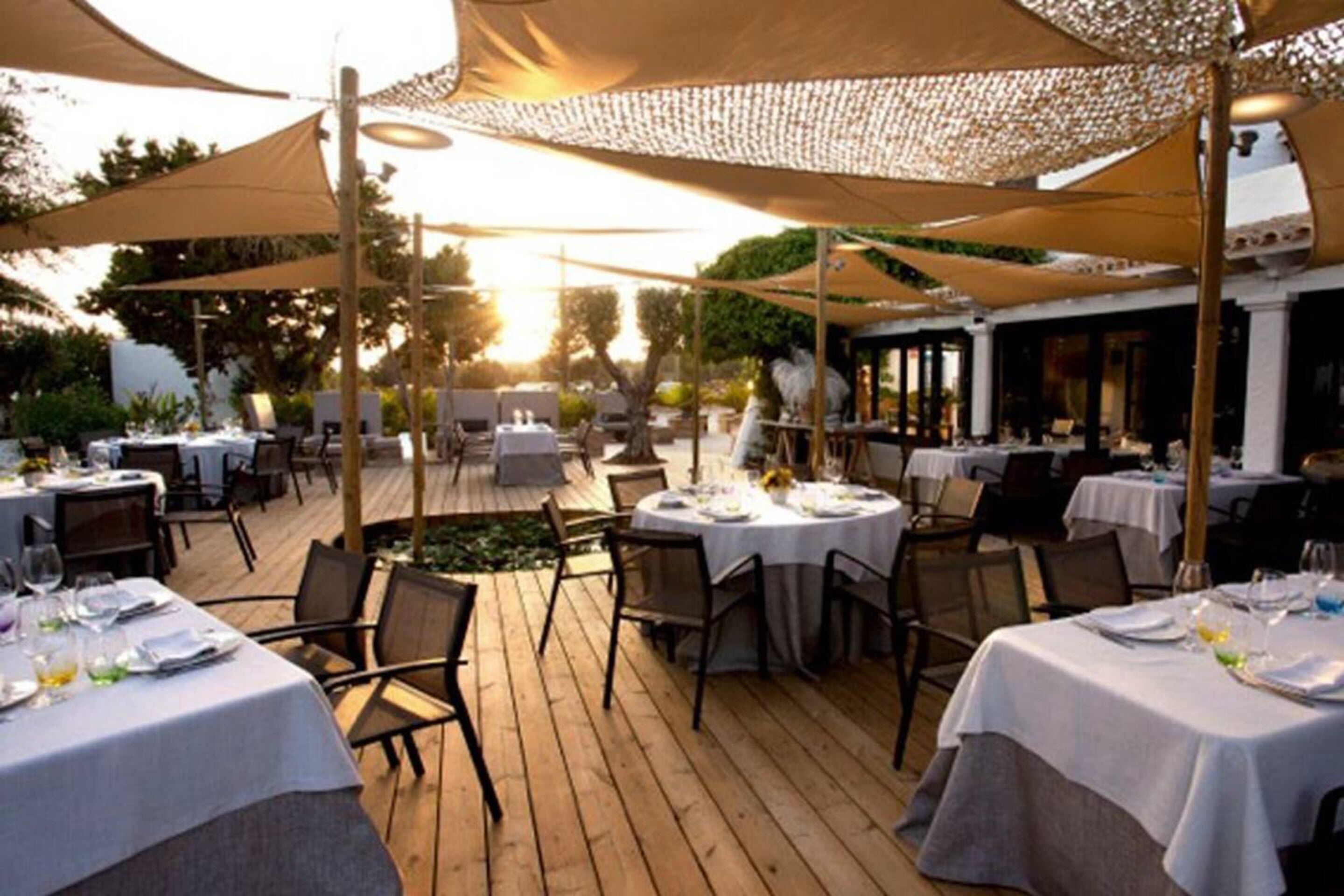 Un área de comedor al aire libre con mesas preparadas para dos, cubiertas por sombrillas grandes y rodeada de cubiertas de madera.