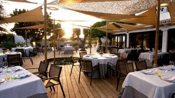Un área de comedor al aire libre con mesas preparadas para dos, cubiertas por sombrillas grandes y rodeada de cubiertas de madera.