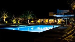 A nighttime swimming pool with lounge chairs and a building with illuminated windows in the background. - Paraíso de los Pinos Apartamentos (Formentera)