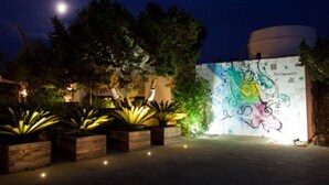 A nighttime outdoor area with a mural, wooden planters, and a building labeled 'Restaurant'. - Paraíso de los Pinos Apartamentos (Formentera)