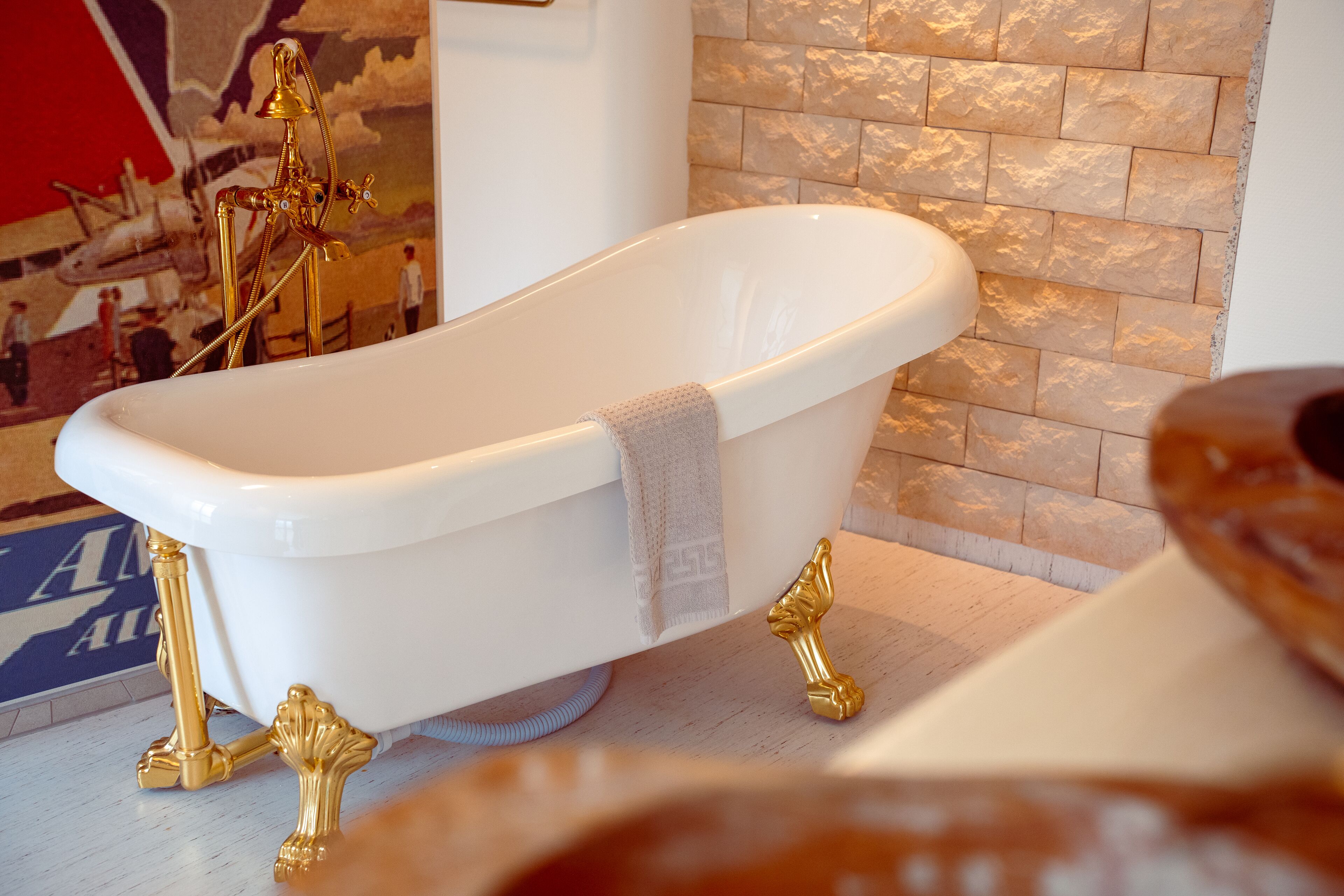 Una vasca da bagno freestanding bianca con dettagli dorati e un asciugamano appoggiato.