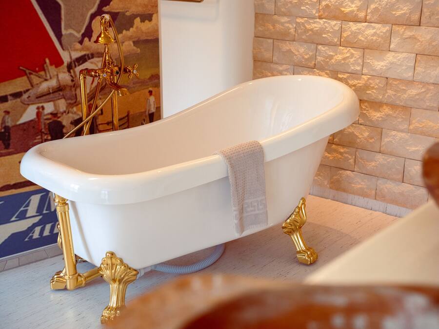 Una vasca da bagno freestanding bianca con dettagli dorati e un asciugamano appoggiato.