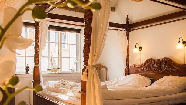 A four-poster bed with a canopy, wooden headboard, and bedside lamps. - Boutique Hotel Postgården (Holsted)