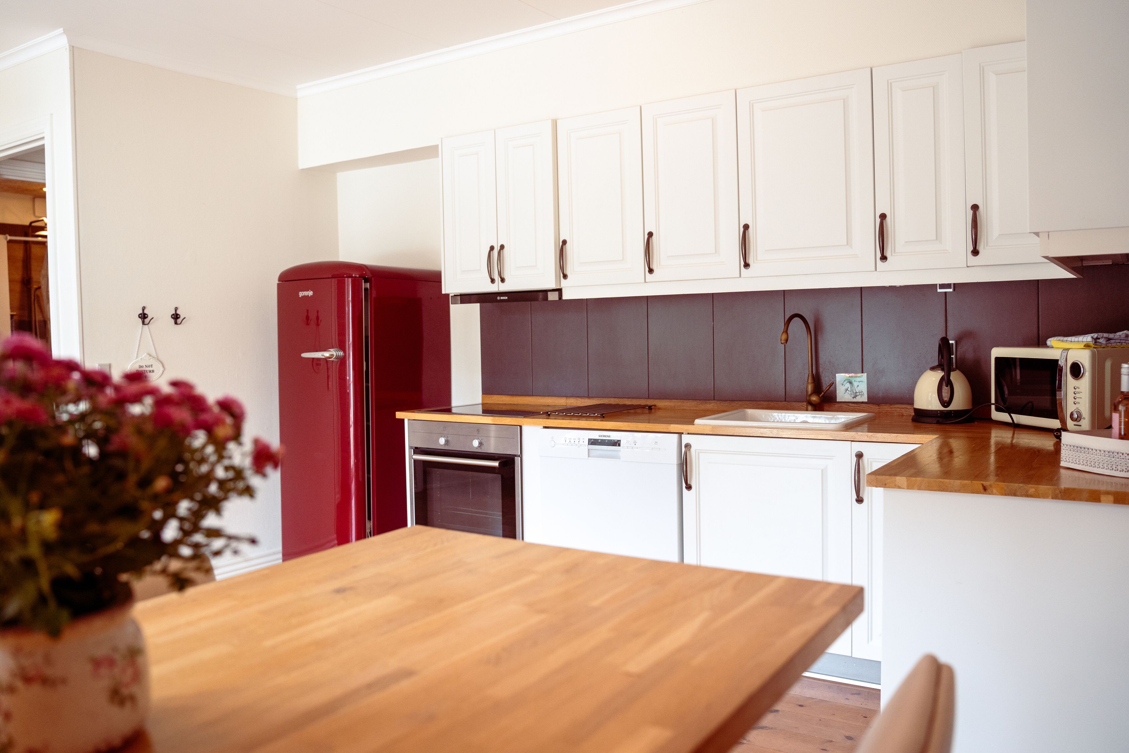 Una cocina moderna con armarios blancos, un refrigerador rojo, una encimera de madera y un microondas.