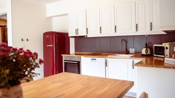 Una cocina moderna con armarios blancos, un refrigerador rojo, una encimera de madera y un microondas.