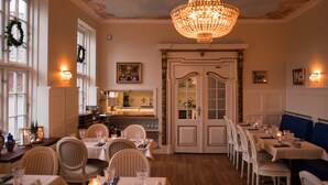 A dining area with tables set for guests, a chandelier, and a view into the kitchen. - Boutique Hotel Postgården (Holsted)