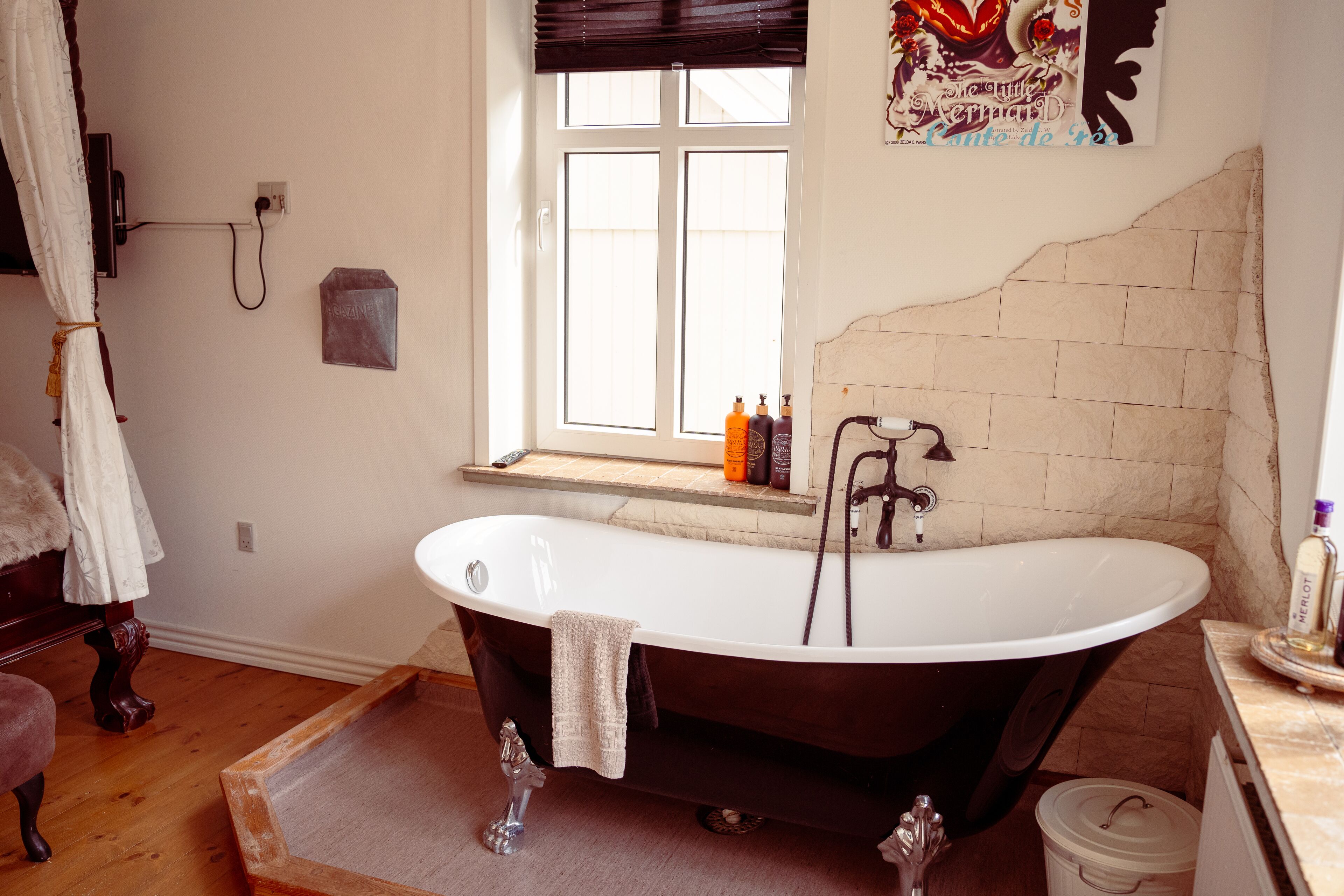 A bathroom with a freestanding bathtub, a window with a view, and a tiled wall.