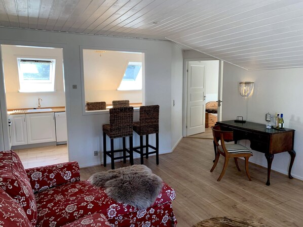 Una sala de estar acogedora con un sofá rojo, un plaid de piel sintética y un comedor con un escritorio de madera y dos sillas de mimbre.