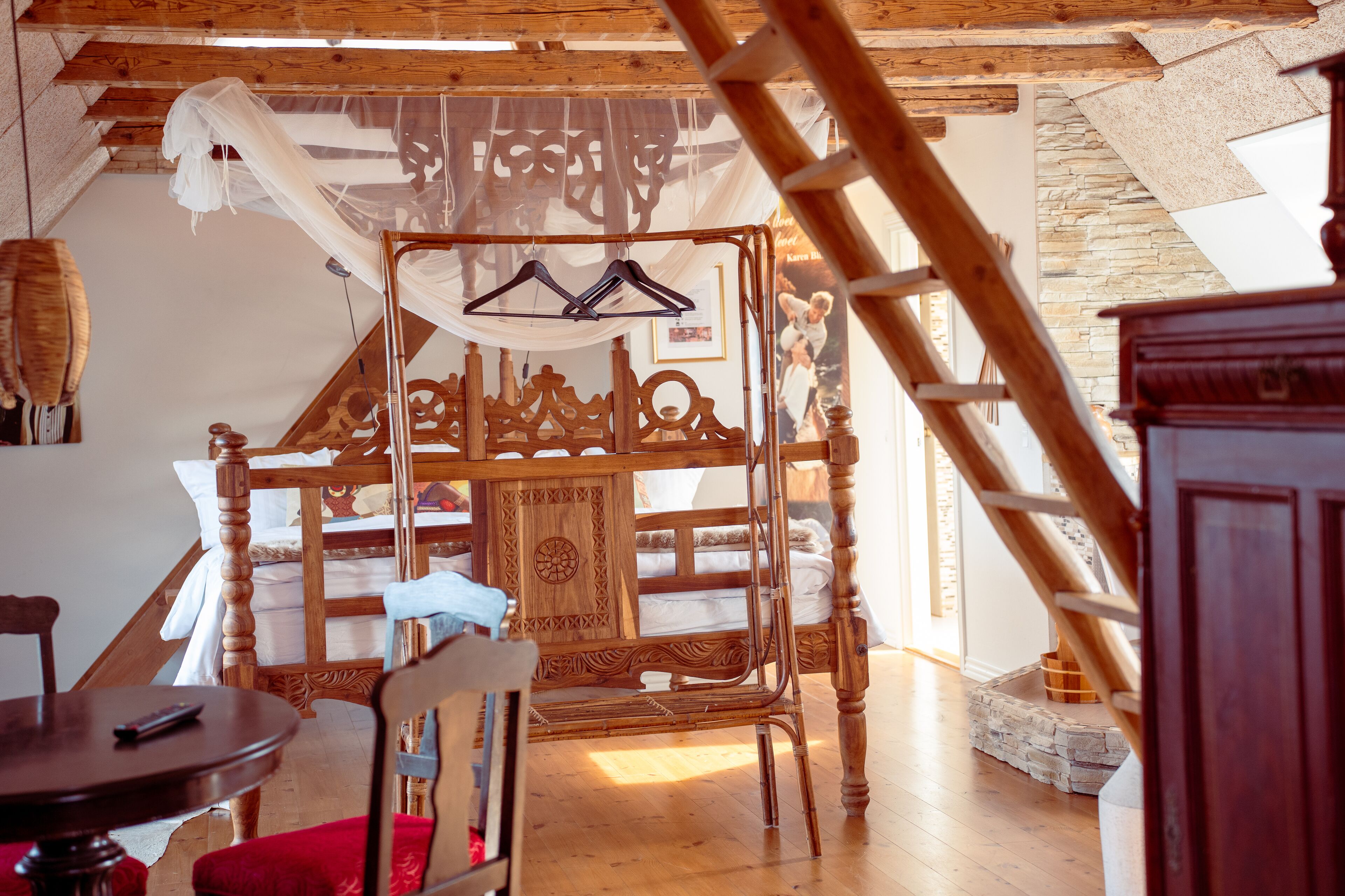 A rustic room with a wooden bed, a chair, a table, and a hanging clothes rack.