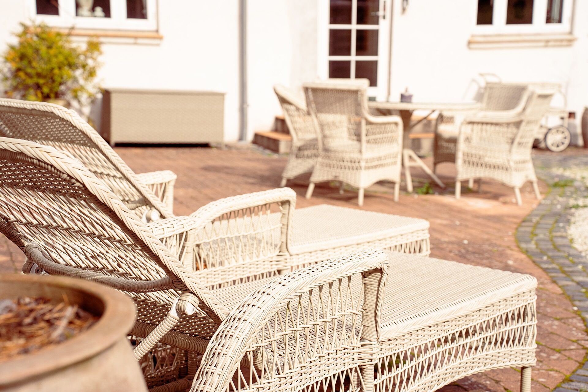 Wicker lounge chairs and a table set on a patio with a white building in the background.