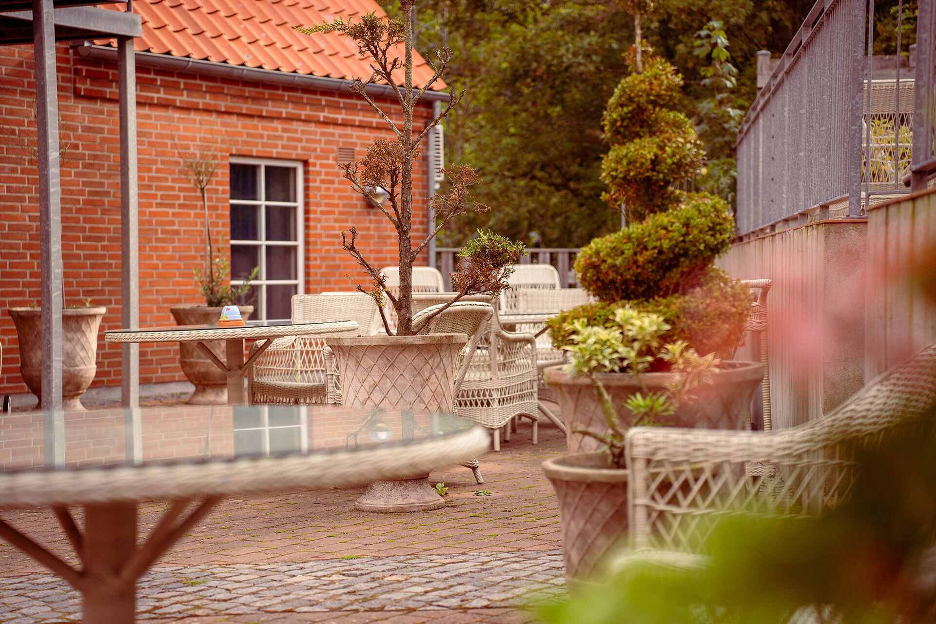 Un patio al aire libre con mobiliario de mimbre, plantas en macetas y un edificio de ladrillo al fondo.