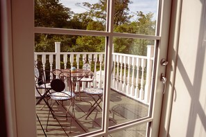A view through a glass door of a patio area with a white railing, a round table, and two chairs. - Boutique Hotel Postgården (Holsted)