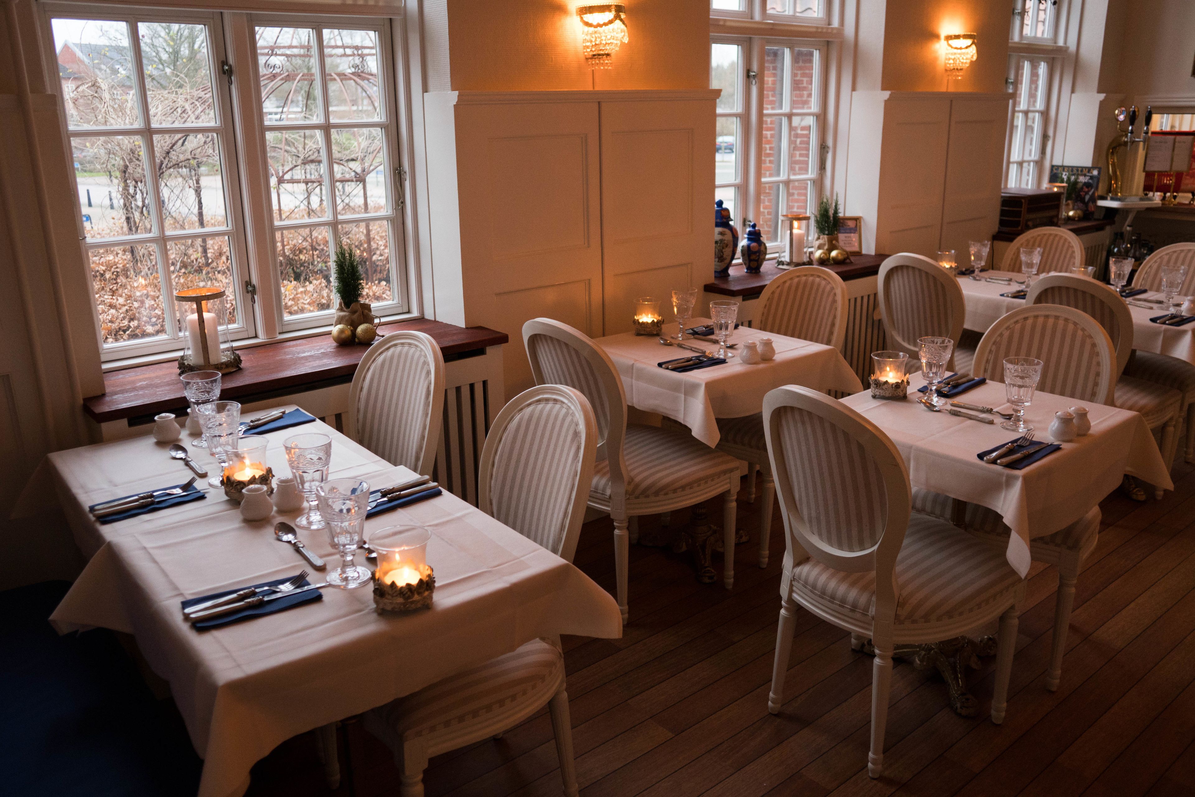 A dining area with tables set for multiple people, featuring white tablecloths, candles, and chairs.