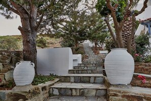 Un escalier en pierre mène à un bâtiment blanc, flanqué de grands vases blancs et d’arbres.