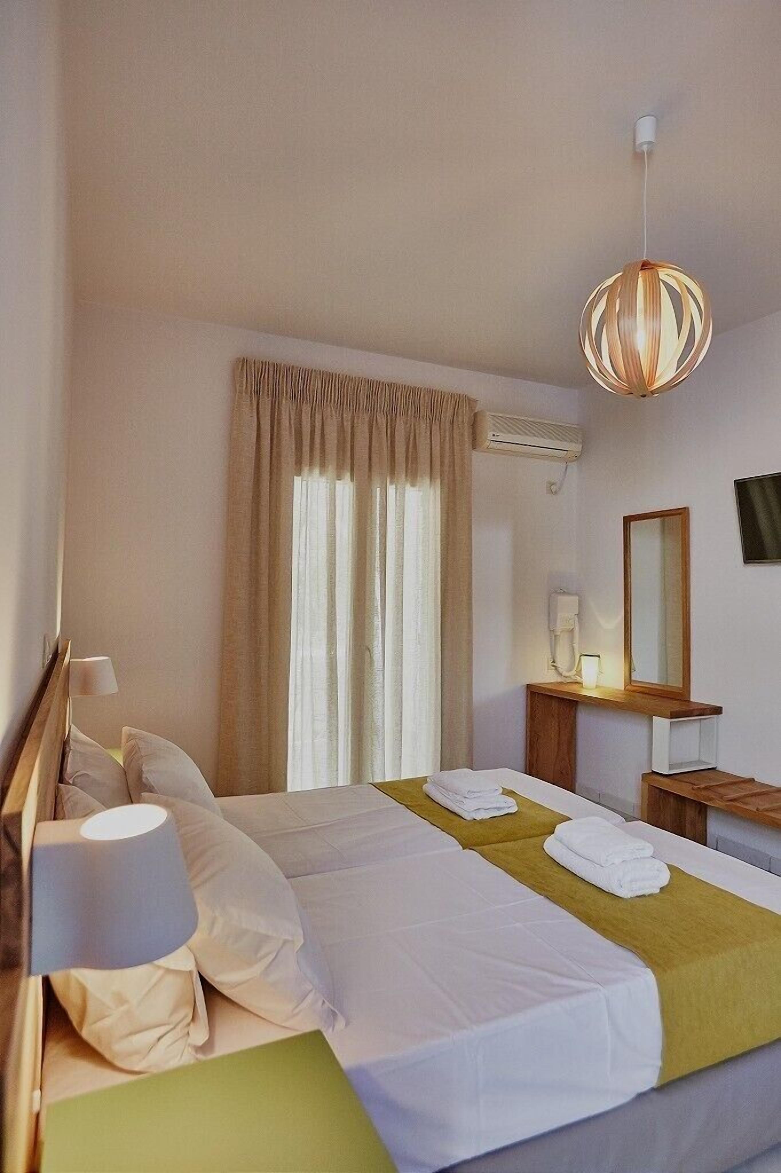 A hotel room with a bed, a bedside table with a lamp, a mirror, and a hanging light fixture.