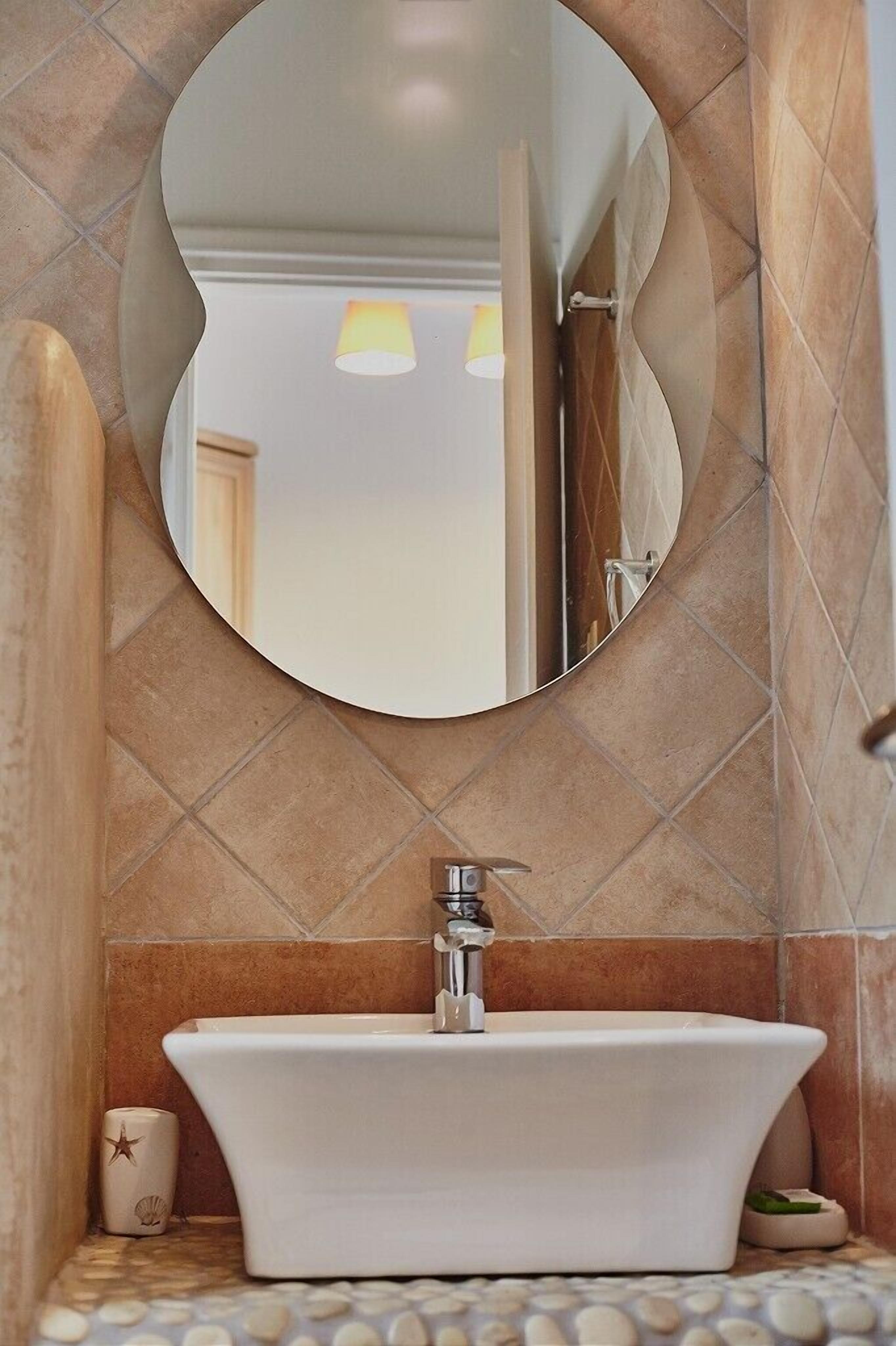 Un baño con una bañera independiente, un espejo redondo y una pared con azulejos.