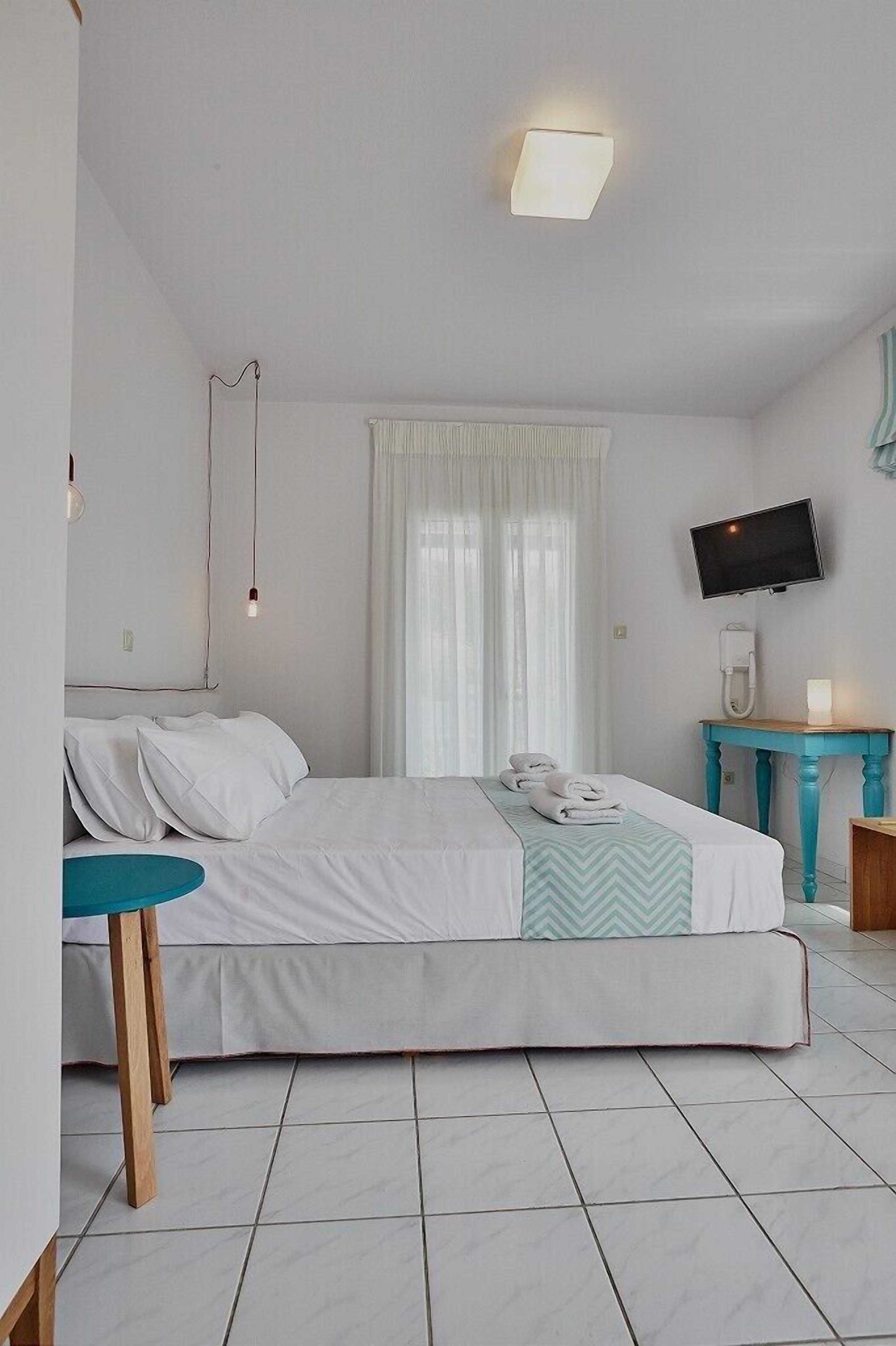 Habitación de hotel con cama, una mesita redonda, televisor montado en la pared y una ventana con cortinas.