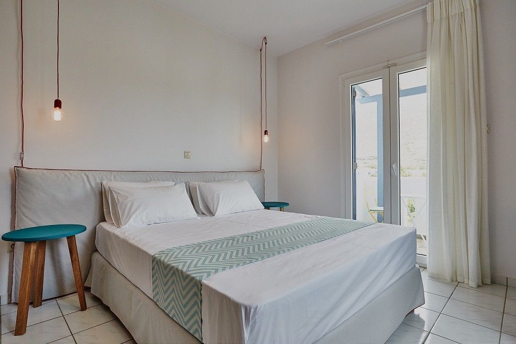 Un dormitorio con cama, dos mesitas de noche, una ventana con cortinas y vistas al exterior.