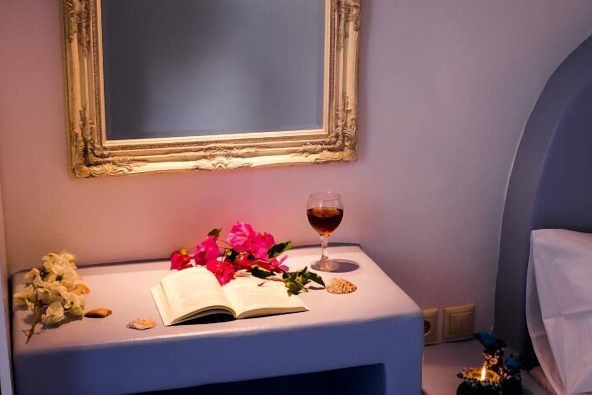 A neatly arranged bedside table with a book, a glass of red wine, and a bouquet of flowers.