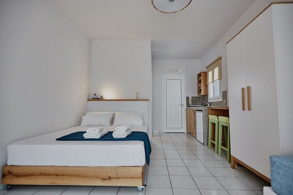 Une chambre à coucher avec un lit, une petite kitchenette et une porte donnant sur une autre pièce.