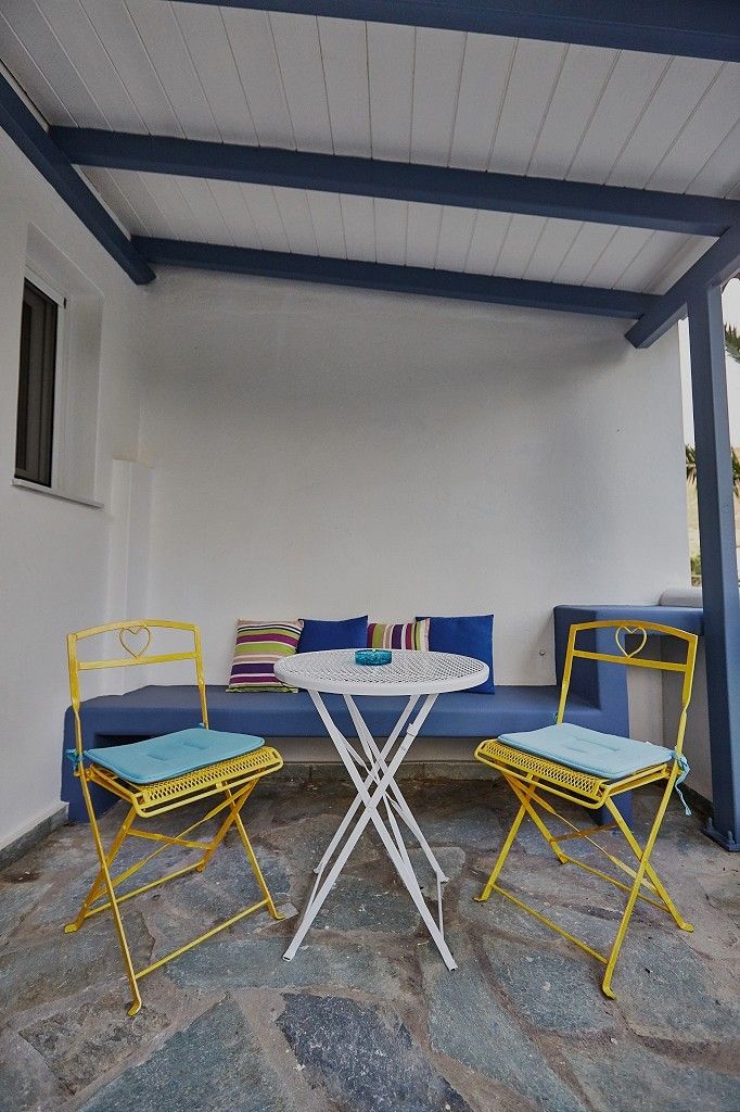 A covered outdoor seating area with a table and two chairs, stone flooring, and a blue and white color scheme.