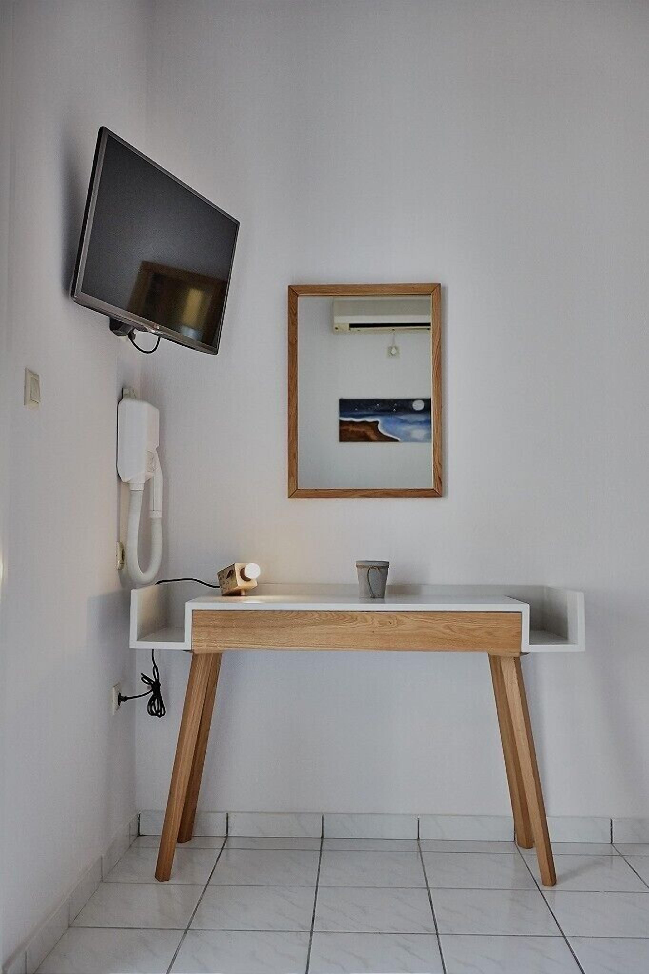 A modern bathroom with a white vanity, wooden legs, a mounted TV, a white telephone, and a framed picture on the wall.