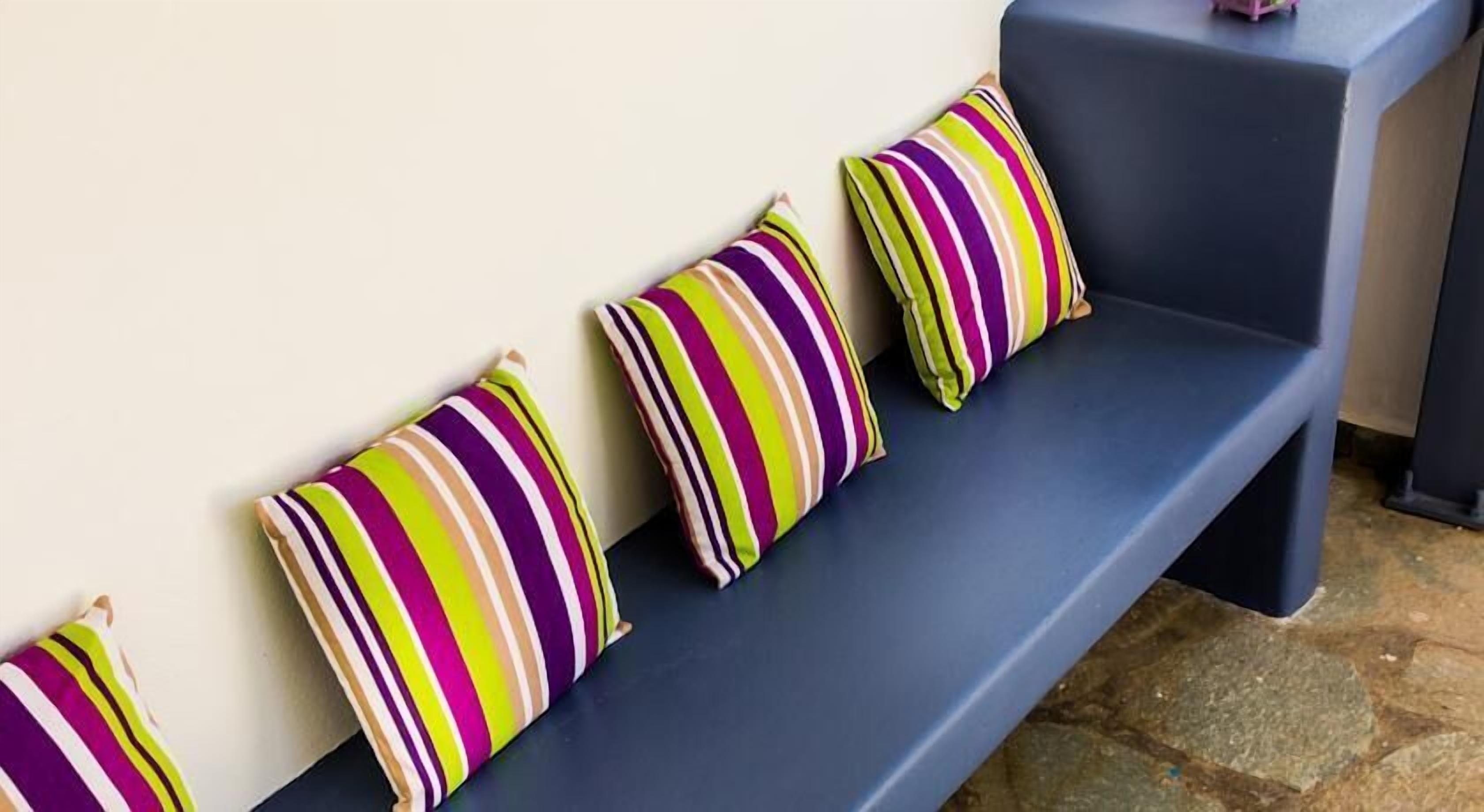 A row of striped pillows on a dark blue bench against a plain wall.