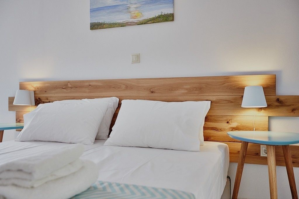 A neatly made bed with white linens and pillows, a wooden headboard, and two bedside tables with lamps.