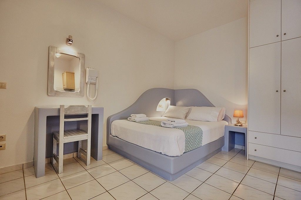 A bedroom with a bed, a bedside table with a lamp, a mirror, and a wardrobe.