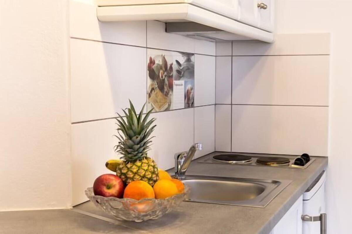 A kitchen with a fruit bowl containing a pineapple, an apple, and oranges on the counter.