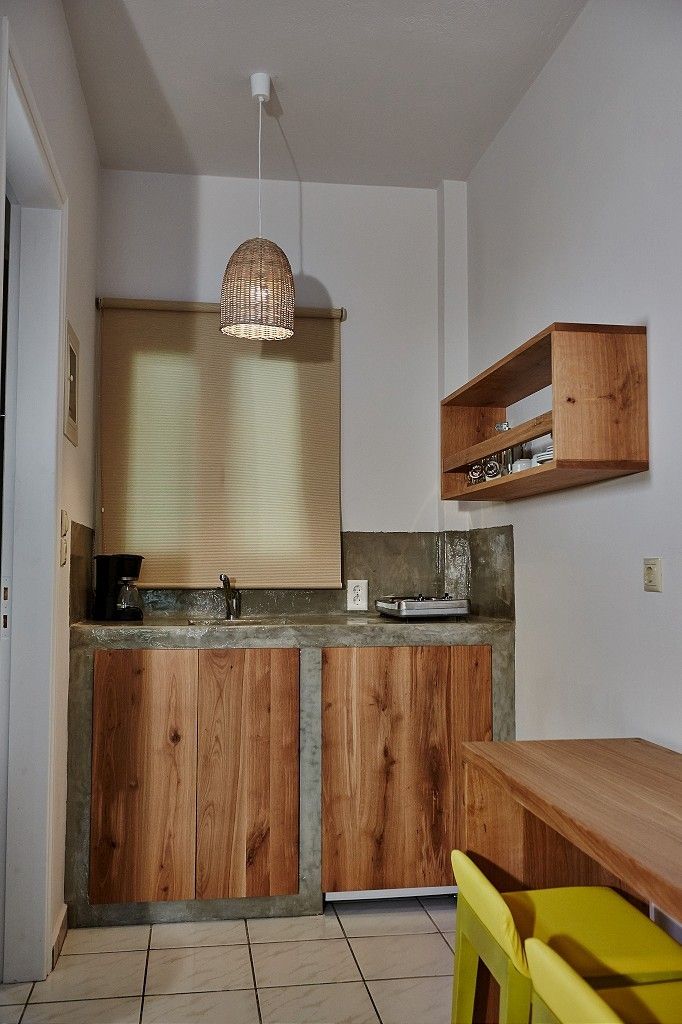 A kitchen with wooden cabinets, a built-in countertop, a hanging light fixture, and a wooden shelf above the counter.
