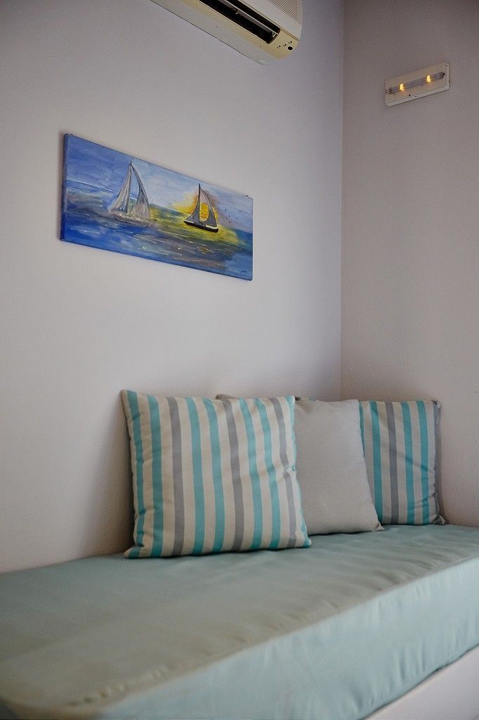 A room with a bed, striped pillows, and a painting of sailboats on the wall.