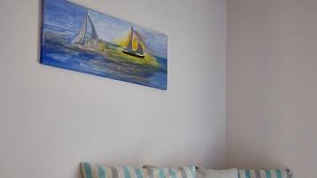 A room with a bed, striped pillows, and a painting of sailboats on the wall.