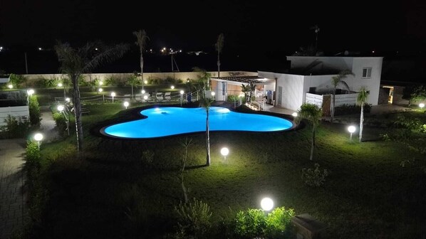 A swimming pool surrounded by a landscaped garden with pathways and lighting.