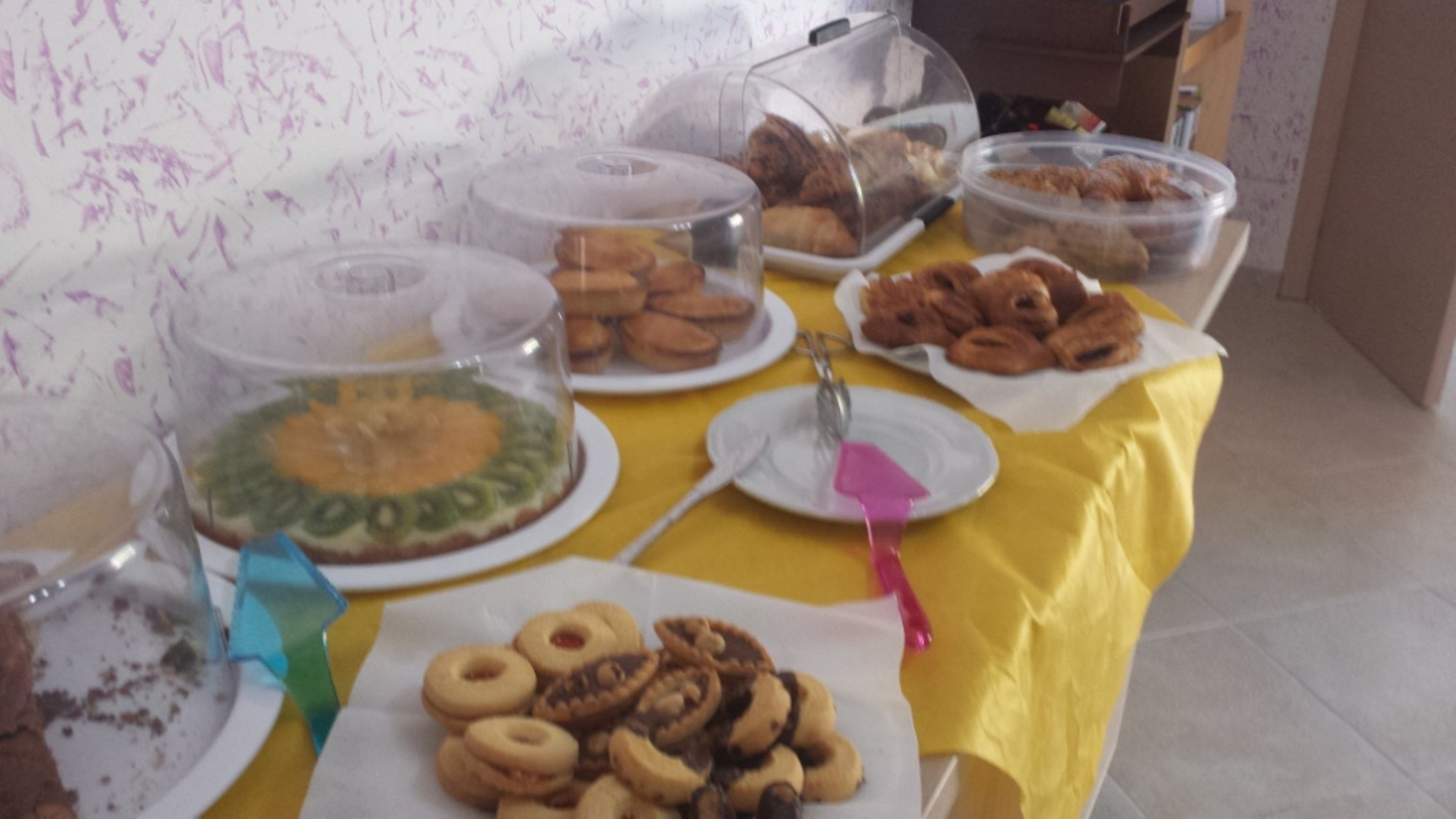 Une table de buffet proposant une variété de plats, notamment des pâtisseries et des desserts, recouverts de cloches en plastique transparent.