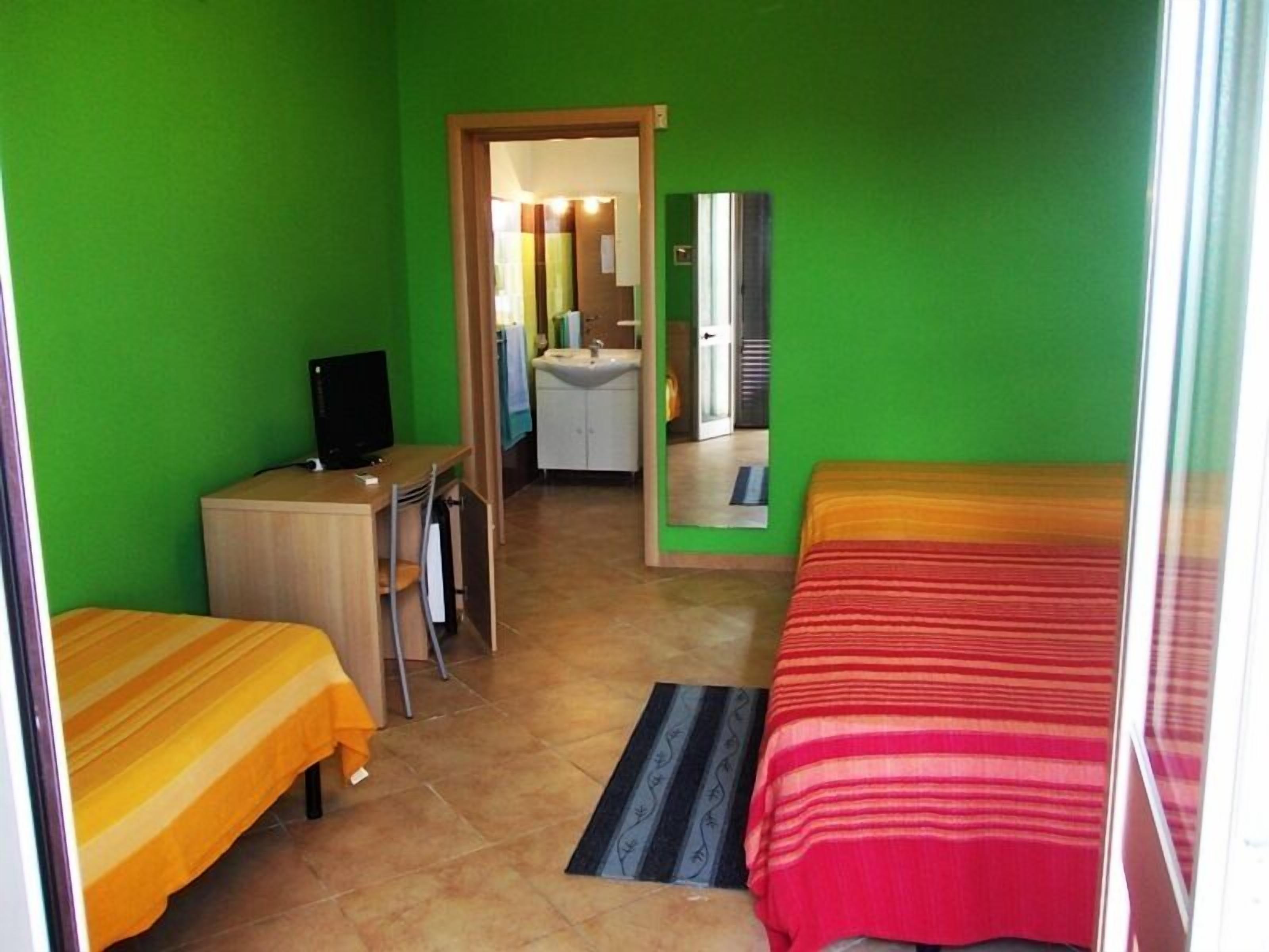 Una habitación con dos camas, un escritorio, un televisor y un baño visible a través de una puerta abierta.