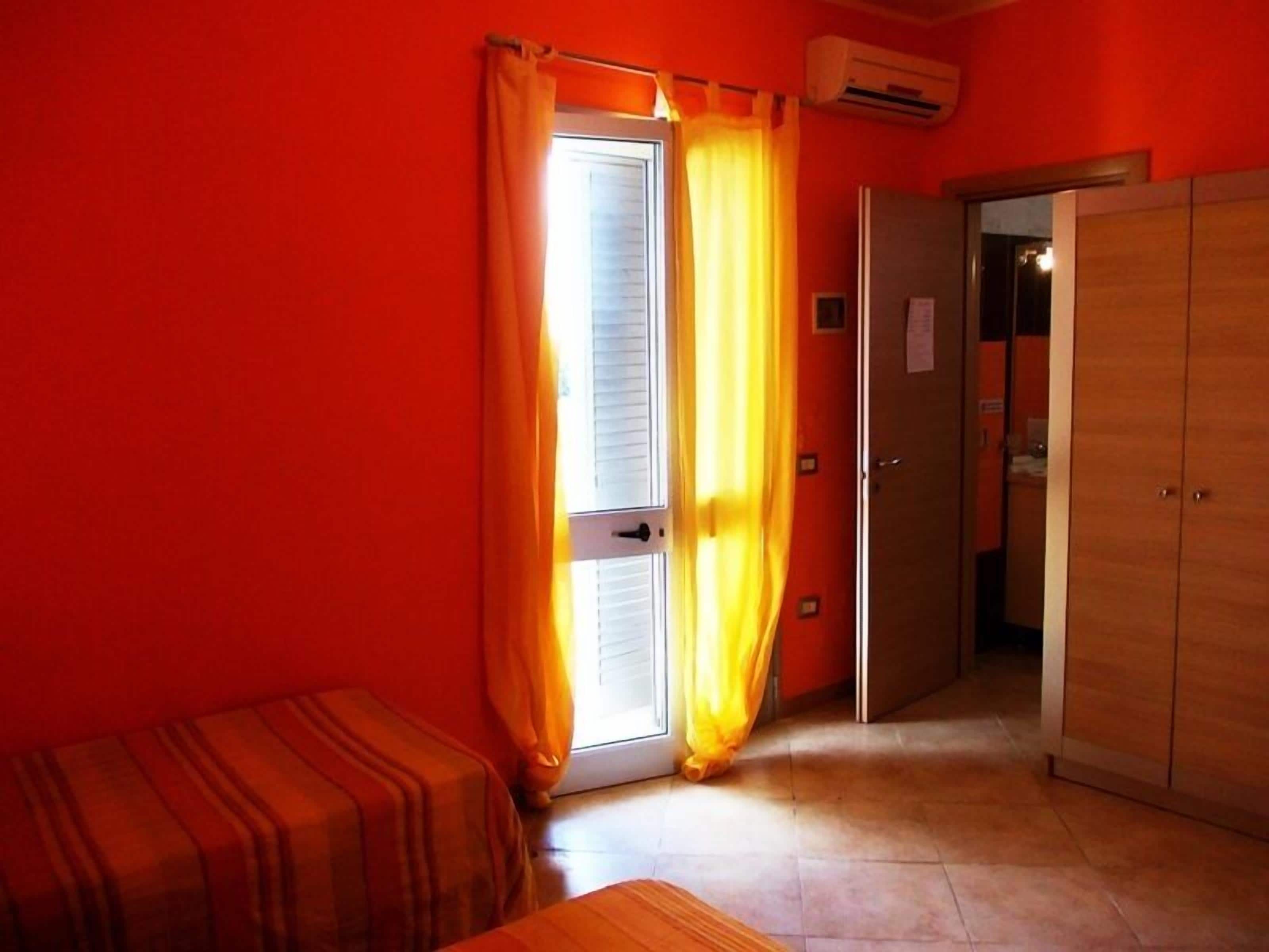 A room with a wooden wardrobe, a bed with striped bedding, and a door with yellow curtains.