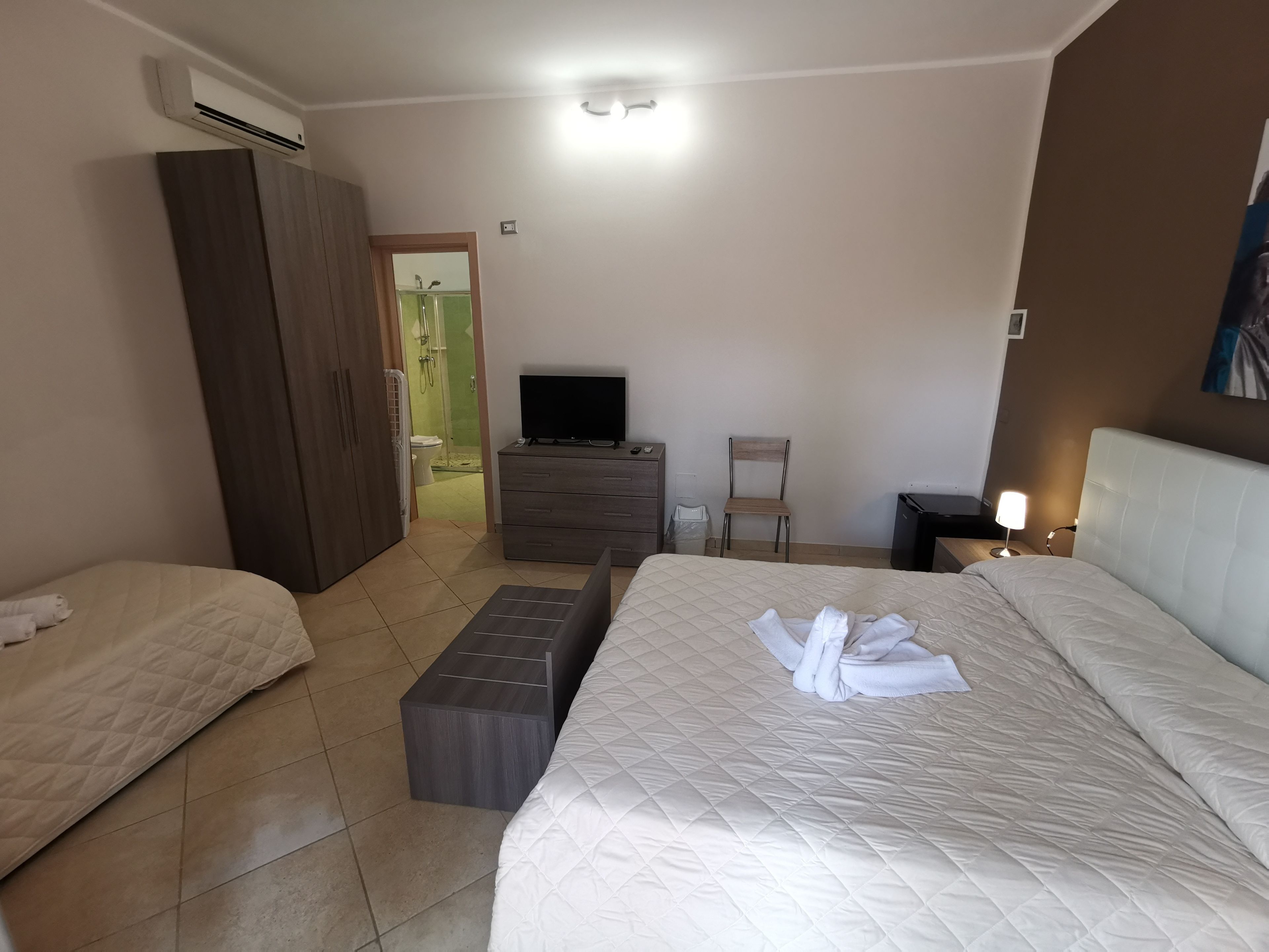 A hotel room with a bed, a TV, a desk, a chair, and an air conditioning unit.