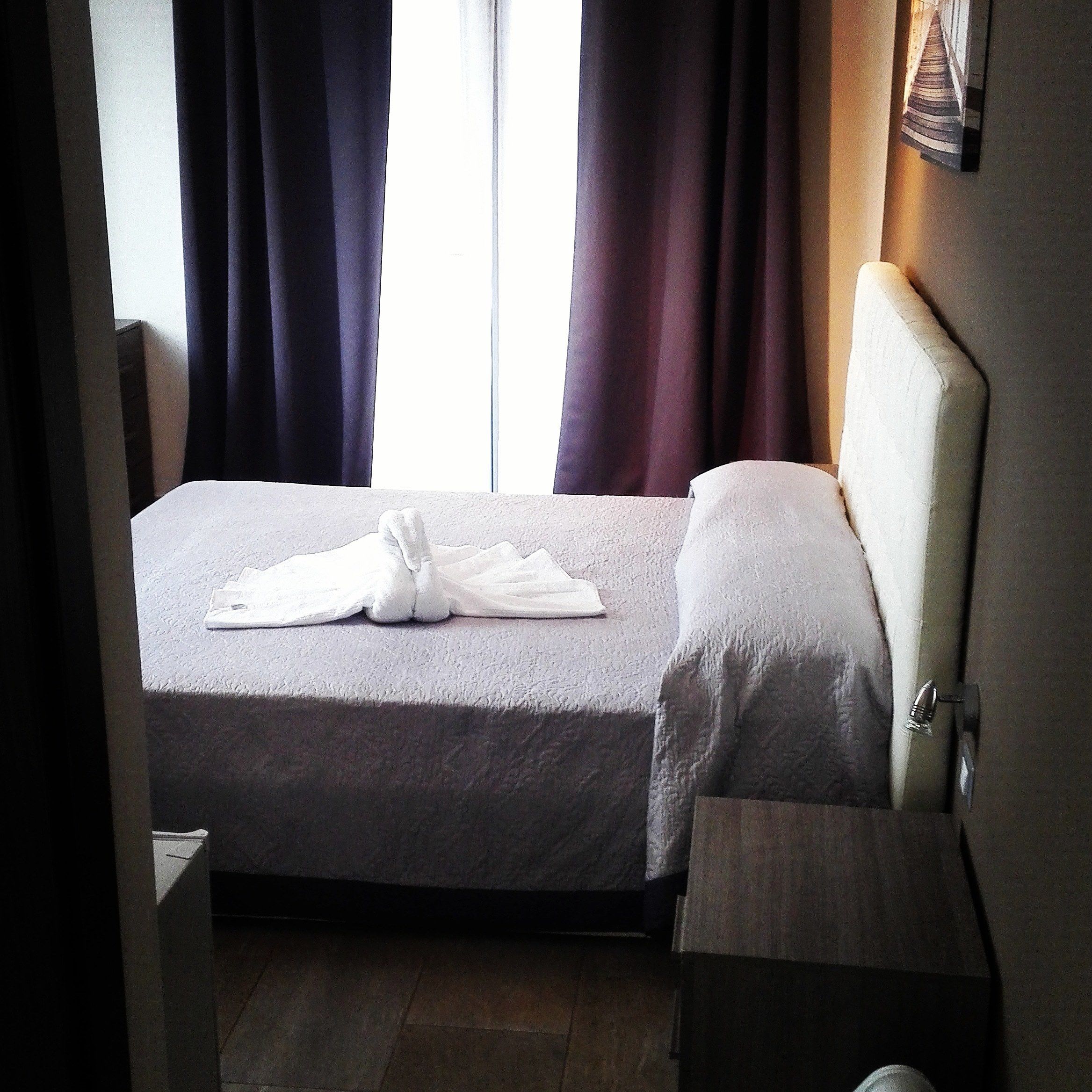 A hotel room with a bed, a bedside table, and a window with curtains.