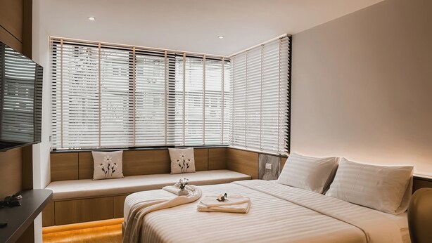 A modern hotel room with a large bed, a bench by the window, and a flat-screen TV. - Townhouse PK Garden (Bangkok)
