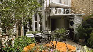 A courtyard with outdoor seating, surrounded by lush greenery and a multi-story building with balconies. - Townhouse PK Garden (Bangkok)